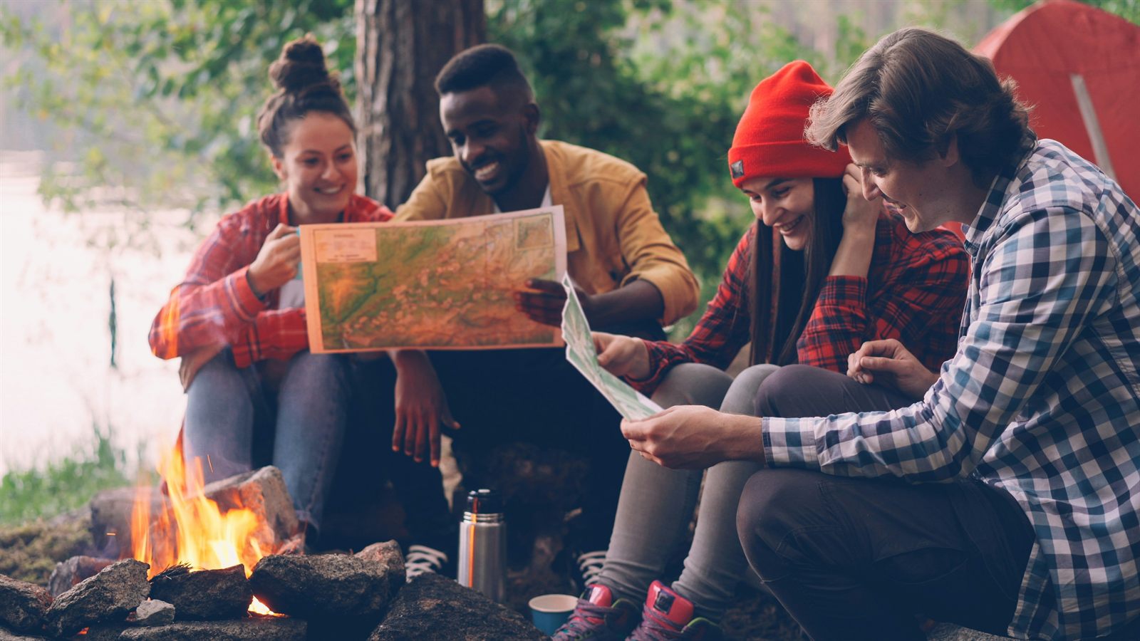 Friends reviewing paper maps together beside a campfire.